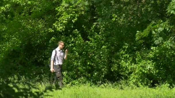 Man met telefoon is wandeltijd Park organiseren een boek toeristische doorbrengen in de natuur onder verse groene bomen zonnige zomer dag Texting klikt op het apparaat — Stockvideo