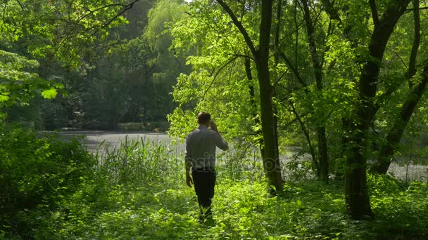 Turistické přichází do parku mluví o telefonu Walking prostřednictvím vysoké trávě v parku zelené stromy čerstvosti ve slunečný letní den slunce muž tráví víkendy na šířku — Stock video