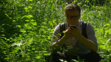 Bir yere park Holding çömelme backpacker yeşil Park tazelik güneş ışığı erkekte dinlenme yemyeşil çim çalılar hafta sonları baharda geçirir telefon