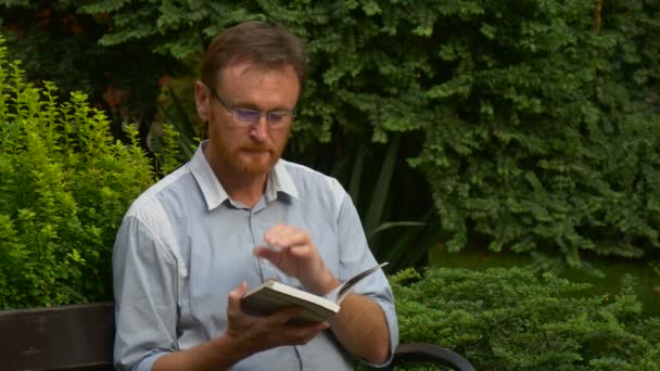 Elderly Man Glasses Reading Book Park Bench Put Book Aside — стокове відео