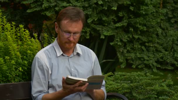 Elderly Man Glasses Reading Book Park Bench Put Book Aside — Vídeo de Stock