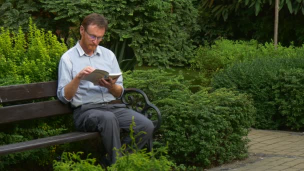 Elderly Man Glasses Reading Book Park Bench Put Book Aside — 图库视频影像