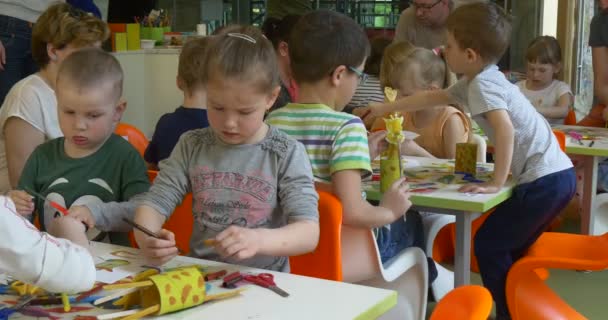 День защиты детей в Ополе Концентрированные дети играют в игрушки из бумаги Жёлтые жирафы Учителя рисования Счастливые дети сидят за столами разговаривая с родителями — стоковое видео