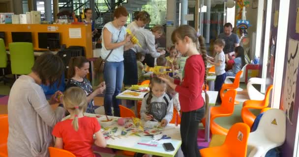 Dia das crianças em Opole Biblioteca Crianças Adolescentes estão fazendo brinquedos Papel Girafas Crianças engajadas em professores de arte Crianças estão sentadas nas mesas com os pais — Vídeo de Stock