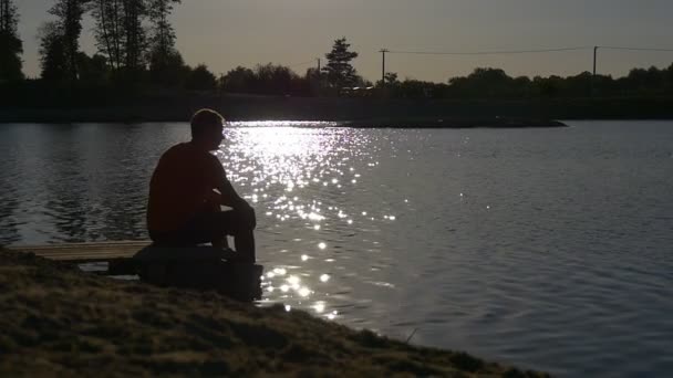 Joven se sienta en la orilla del río — Vídeo de stock