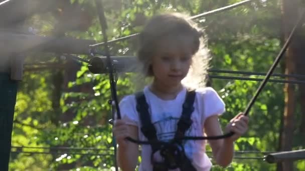 Ragazza è in Adventure Rope Park è Summer Day Bambino si diverte Occupato da Sport Kid è fissato con cinture di sicurezza a piedi con attenzione Sunny Weather Green Trees — Video Stock