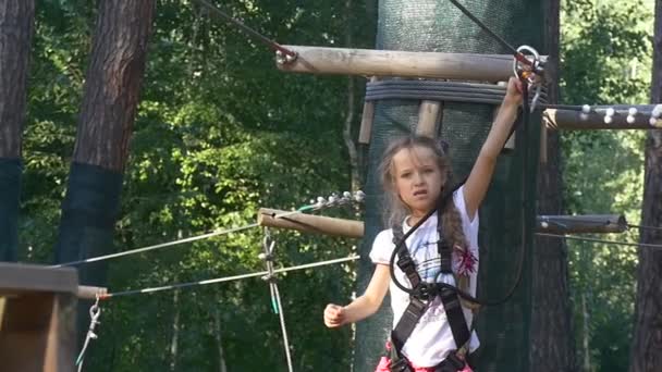 Chica cierra una carabina en un cable de metal aventura cuerda Park Instructor va a ayudar a los niños verano soleado día niño se divierte ocupado por el deporte en la naturaleza — Vídeo de stock