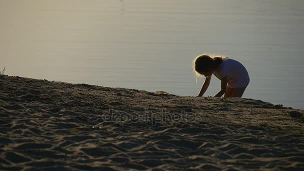 Petite fille blonde creuse un trou dans un sable — Video