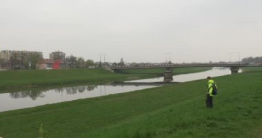 Nehir manzara adam açık havada Cityscape bir ufuk araba köprüde bulutlu Nehri üzerinde dinlenme yeşil çim üzerinde yakınındaki turistik sarı ceketli oturur