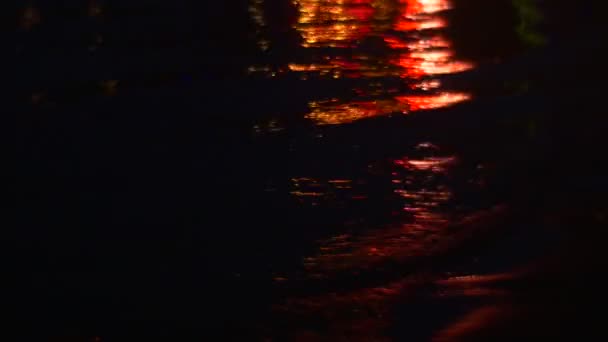 La reflexión roja sobre las olas se cambia a púrpura, luego azul, amarillo. Noche en el río, la playa, los ecos de la discoteca — Vídeo de stock