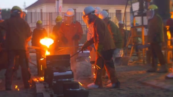 Hombres vertiendo metal líquido Fundición de hierro en los trabajadores del atardecer cerca de la fundición del horno al aire libre Festival de altas temperaturas en Wroclaw Personas en Cascos Ropa de trabajo — Vídeos de Stock