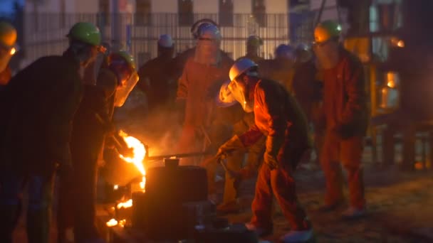 Показати на фестивалі високих температурах у Вроцлаві чоловіків у шоломи виливаючи рідкого металу на відкритому повітрі біля печі виступ на ніч міський пейзаж — стокове відео