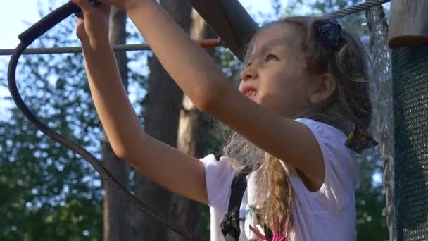 Маленька дівчинка ремонтує ліс кріплення пригод мотузковий парк влітку сонячний день ліс щаслива дівчинка з довгою косою дитина весело зайнята спортом — стокове відео