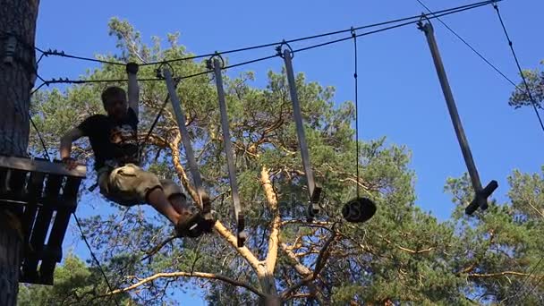 Tourisme ne parvient pas à marcher par des escaliers de corde dans l'aventure Le jeune homme sourit s'amuse dans le parc de jour d'été Promenade par la route de corde Grumes en bois Tourisme en Ukraine 