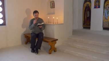Noel Svyatogorsk Manastırı adam İncil kilise mum resimleri simgeleri vardır üzerinde duvar tapan ışığında bankta oturuyor okuyor