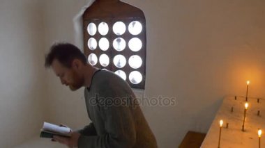 tarafından Absorbedly Svyatogorsk turizm Ukrayna için tebeşir mağara tur içinde kilise Şapel içinde kitap turizm Holding okuma mumlar yaktı bir mağarada bir adam dua ediyor