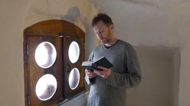 Homem na Janela Com uma Bíblia em Sua Mão Crente está Lendo Em Voz Alta Caminhando Por Quarto Meditando Igreja Ortodoxa Mosteiro Pequena Janela De Madeira Quadro — Vídeo de Stock