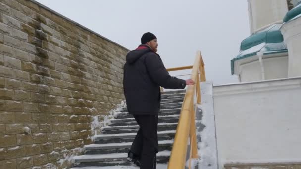 Muž lezení nahoru schody Svyatogorsk lávře zimní krajina svaté hory lávře jeskynní klášter zataženo zasněžené den turistické na pravoslavné církevní stavby — Stock video