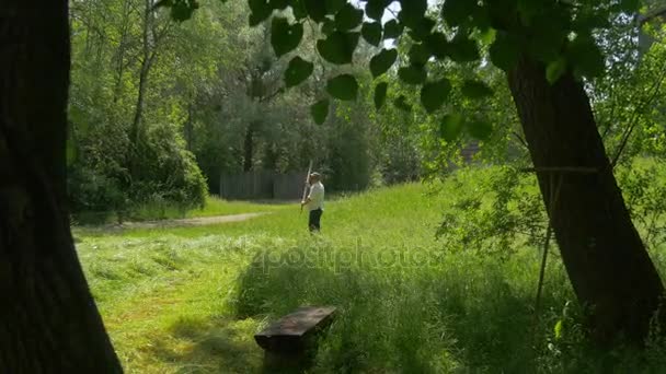 Kindertagsarbeiter mäht grünes Gras ländliche Landschaftshütten im Park der alten polnischen Architektur Windmühlen Ethnographisches Museum in sonnigem Sommertag — Stockvideo