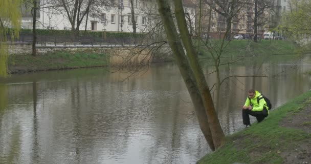 Dark-Haired Man Sits on Shore of a Small River — Stock Video