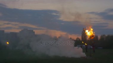 Erkekler yangın siluetleri çevresinde yangın Dusk gösteriler üzerinde kenar, şehir konut evler yeşil çayır bahar akşam günbatımı pembe Sky yanar