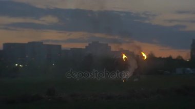 Siluetleri bisikletçi ata duman ile cesur askerler ateş alacakaranlıkta gösteriler şehir konut evler yeşil çayır bahar kenarında akşam