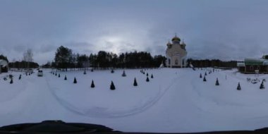 360 vr Video 360 Degrees. Man Walks by Trampled Snow to Orthodox Church of the Holy Elijah in Slavutich City, Ukraine. Cameraman is Taking Video of His Way. Decorative Small Evergreen Trees Along the Alley. Field is Covered by Snow. no People