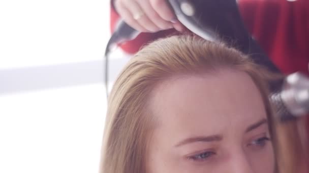 Stylist está adicionando volume aos cabelos Tratamento Profissional Cabeleireiro está usando secador para loira Cliente Feminino Como fazer o cabelo liso brilhante e saudável — Vídeo de Stock