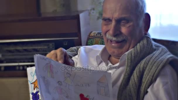 Homme âgé parmi l'intérieur vintage de sa chambre Grand-père tient des dessins de ses petits-enfants et raconte une histoire drôle Souvenirs doux Vieil homme sourit — Video