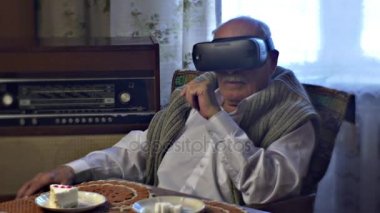 Yaşlı adam görünüyor vr gözlük işaret bir şey oynamak oyun alır ile kulaklık kapalı oturan tablo kaplı ile örgü masa örtüsü, hayal kırıklığına