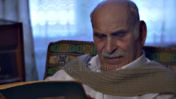 Starší muž je, že čtení knihy pozorně životní příběh dědeček je sedět v pohodlné křeslo a těší sladké vzpomínky Vintage interiéru z útulné pokoje — Stock video