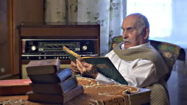 Großvater 80 Jahre alt liest eine alte Wohnzimmer väterlicherseits alte Bücher sind auf einem Tisch Besucher hören Memoiren eines alten Mannes Familienwerte — Stockvideo