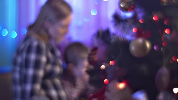 Die Nacht vor Weihnachten glückliche Familie liest Märchen feiert Feiertage hinter bunt geschmücktem Neujahrsbaum zu Hause genommen schwangere Mutter Sohn — Stockvideo