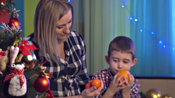 Mutter und Sohn halten Früchte Zitrusfrüchte Heiligabend zusammen Blaulichter schmücken das Zimmer der Menschen glückliche Familie feiert Feiertage winterlichen Urlaub zu Hause — Stockvideo