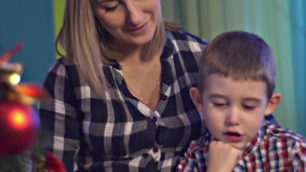 Kleine jongen houdt lezing met Mom at Home kerstavond vrouw is zwanger Happy familie viert vakantie samen warme gezellige kamer winterse avond — Stockvideo