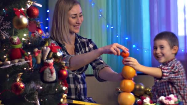 Mamá e hijo juegan construyendo pirámide de frutas cítricas naranjas Navidad Noche invernal en casa Los niños necesitan tiempo Amar a la familia juntos Luces azules Abeto decorado — Vídeos de Stock