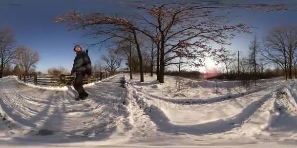 360vr videóinak hátizsákos forgatás falu vidéki téli táj hideg napsütésben kék óra lövés kék ég csupasz ág fák letaposott hó kiterjed az út — Stock videók