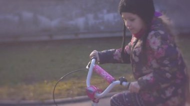 Küçük kız soğuk sonbahar ya da kış gününde bisiklet sürüyor.