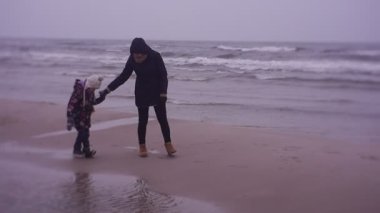 Mother and daughter walking on sea coast in cold weather