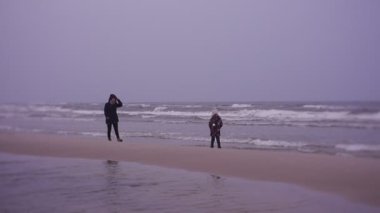 Mother and daughter walking on sea coast in cold weather