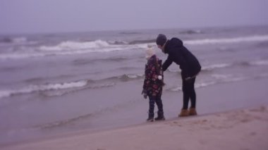 Mother and daughter walking on sea coast in cold weather