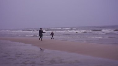 Mother and daughter walking on sea coast in cold weather