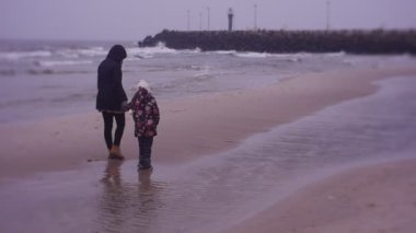 Mother and daughter walking on sea coast in cold weather