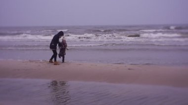 Mother and daughter walking on sea coast in cold weather