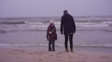 Mother and daughter walking on sea coast in cold weather