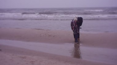 Mother and daughter walking on sea coast in cold weather