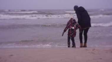 Mother and daughter walking on sea coast in cold weather