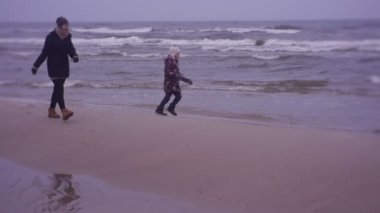 Mother and daughter walking on sea coast in cold weather