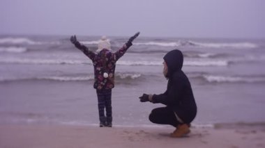 Mother and daughter walking on sea coast in cold weather