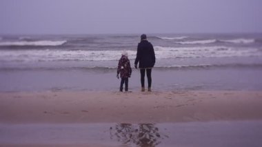 Mother and daughter walking on sea coast in cold weather